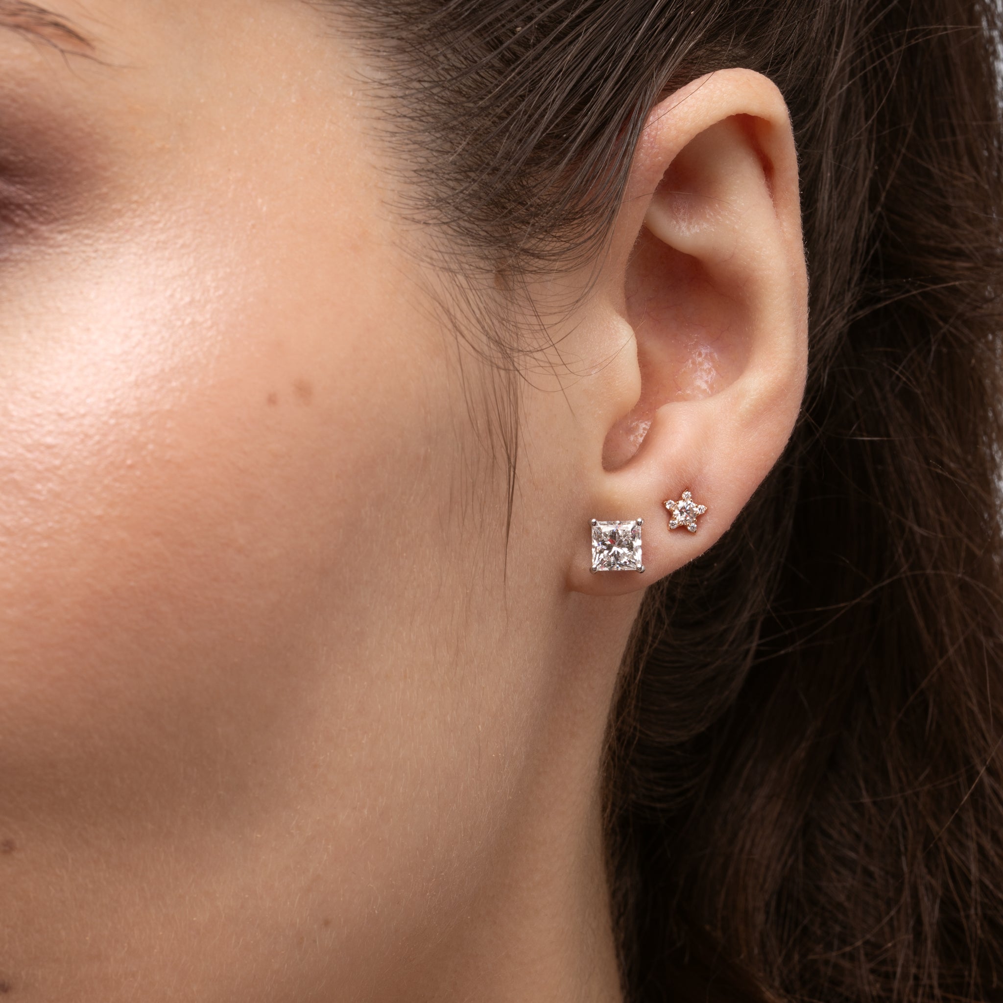 Close-up of an ear wearing a princess cut diamond stud earring with a blurred background