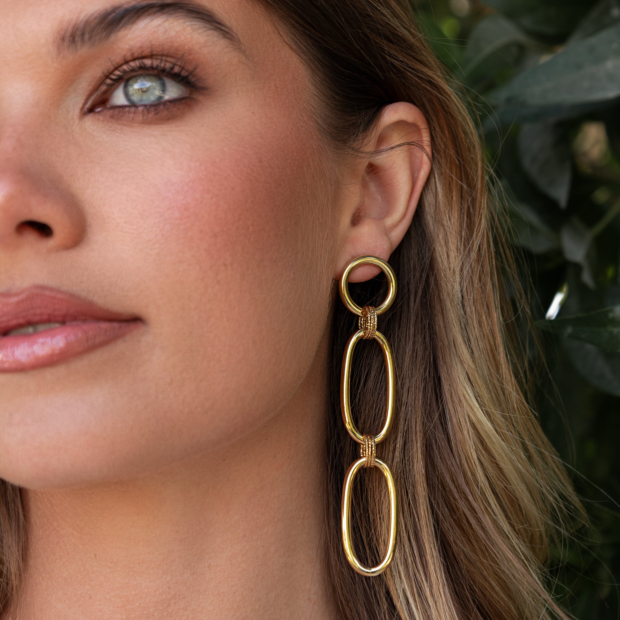 Close-up of a woman wearing gold earrings with a blurred green background