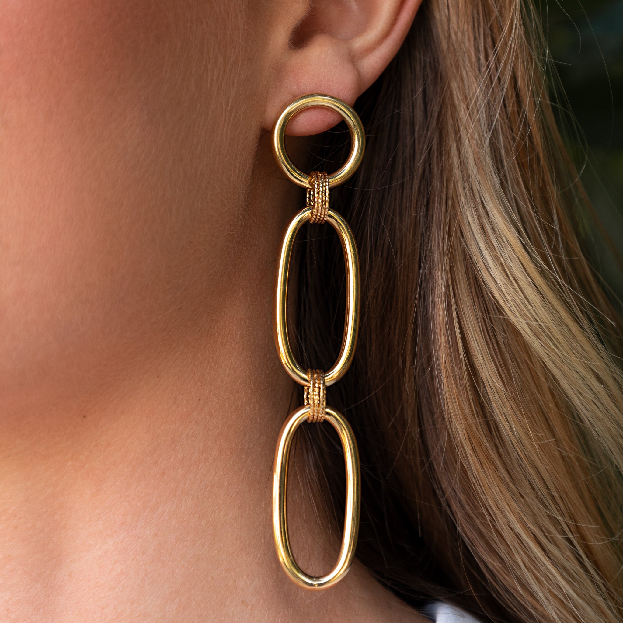 Gold chain earring worn by a person with blonde hair.