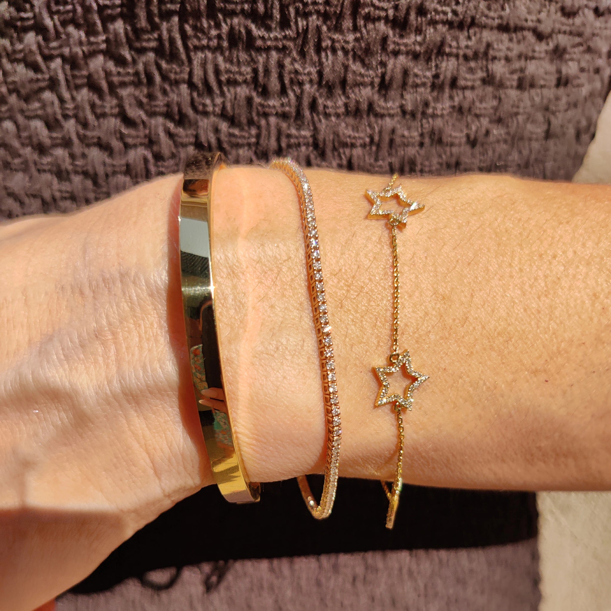 Close-up of a hand wearing a diamond star bracelet on a delicate chain with a golden cuff and sparkly bangle.