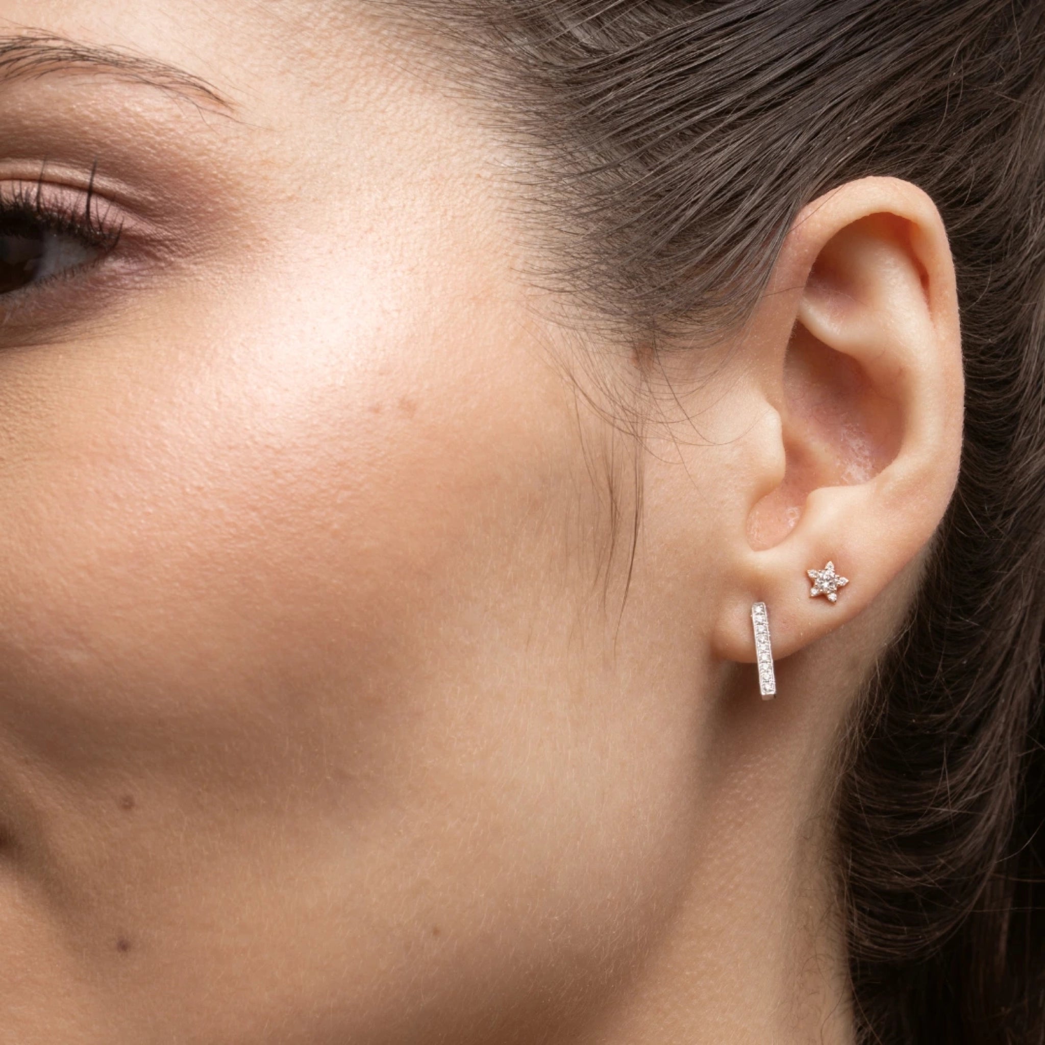 Close-up of a woman's ear featuring certified diamond earrings, showcasing a star design with sparkling diamonds.