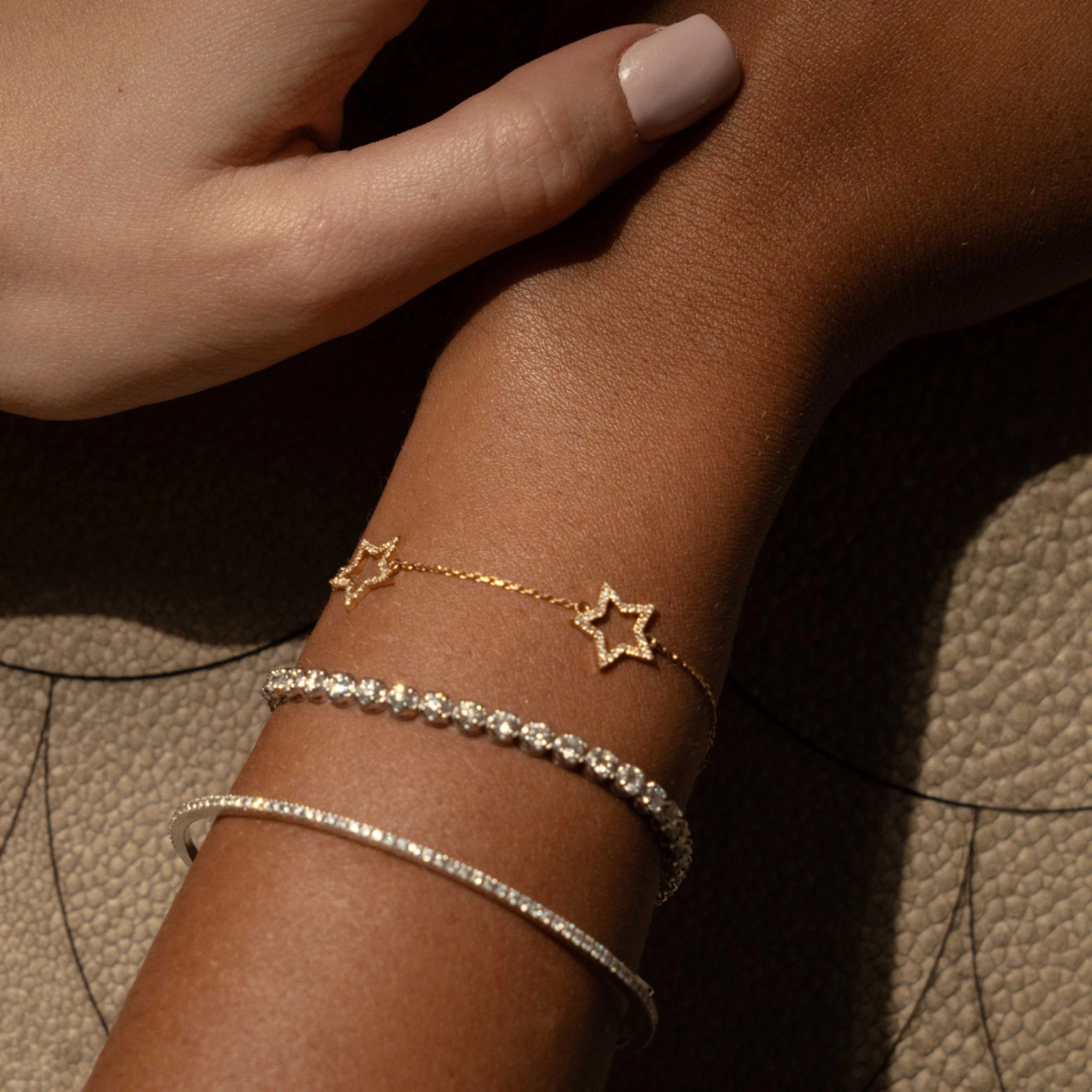 Close-up of a hand wearing a star diamond bracelet alongside two elegant bangles on a textured surface.