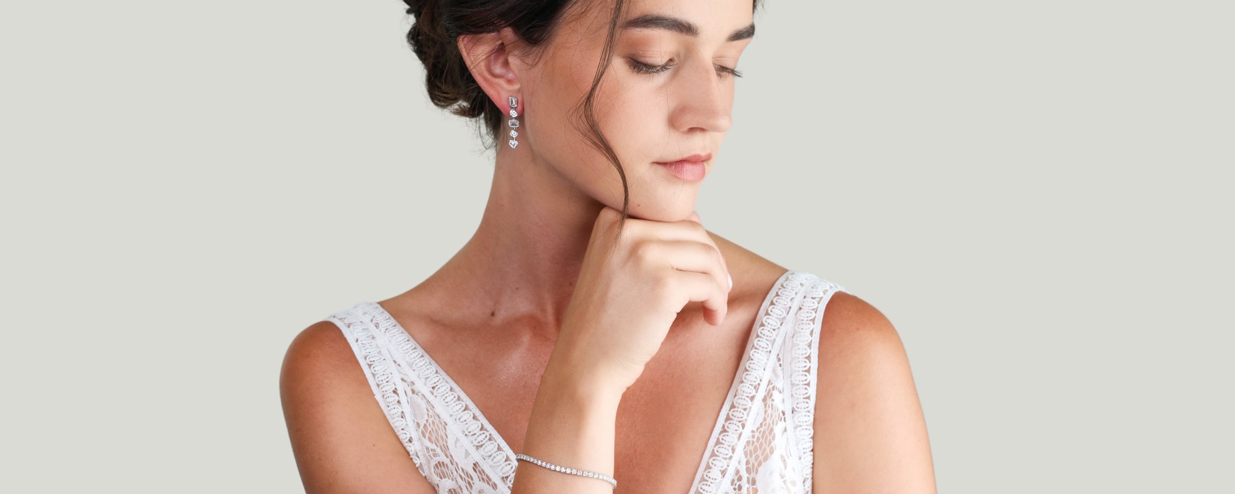 A woman wearing a white lace-trimmed wedding dress, a delicate diamond tennis bracelet, and diamond earrings