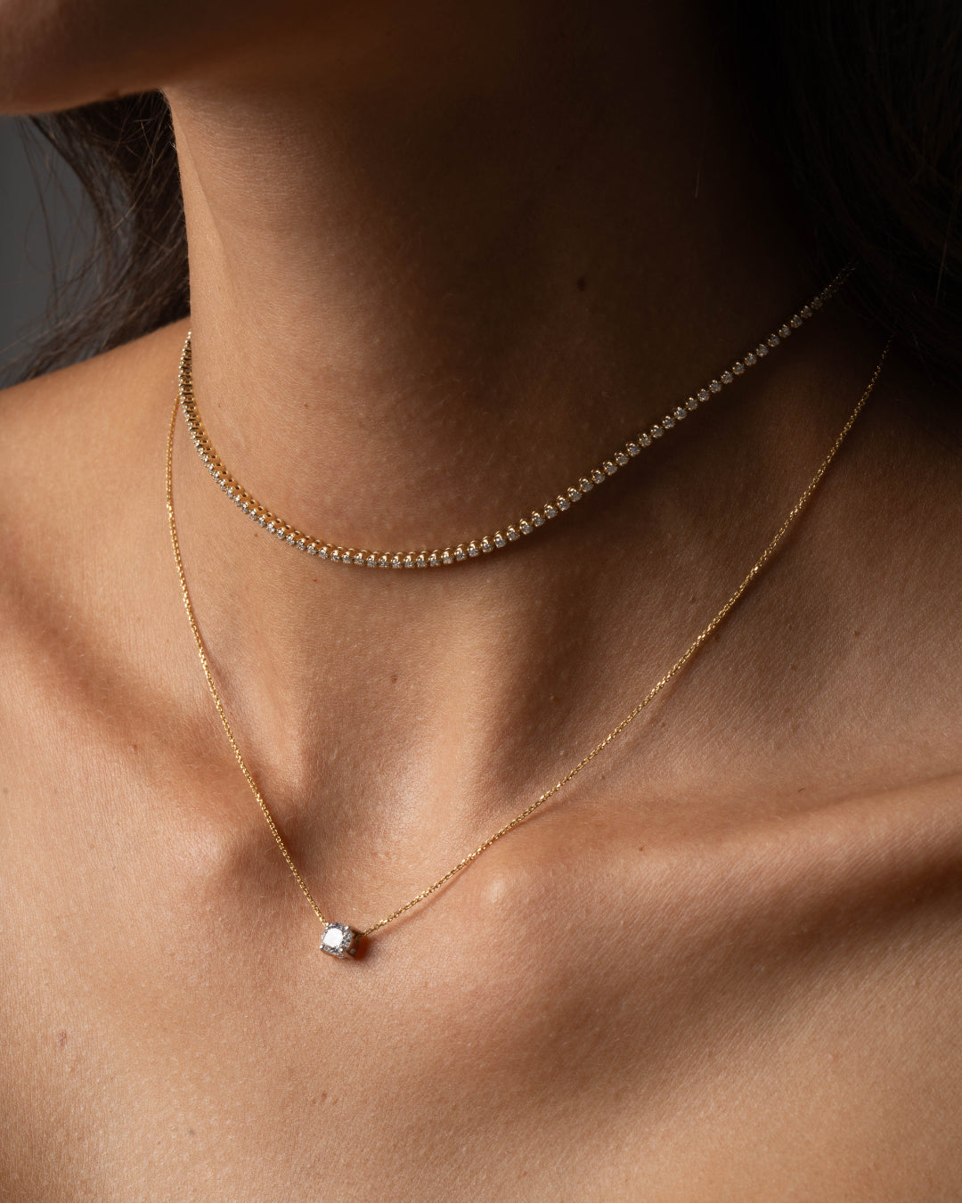 Close-up of a woman's neck featuring The Floating Diamond Necklace paired with a delicate choker, showcasing elegant gold accessories.