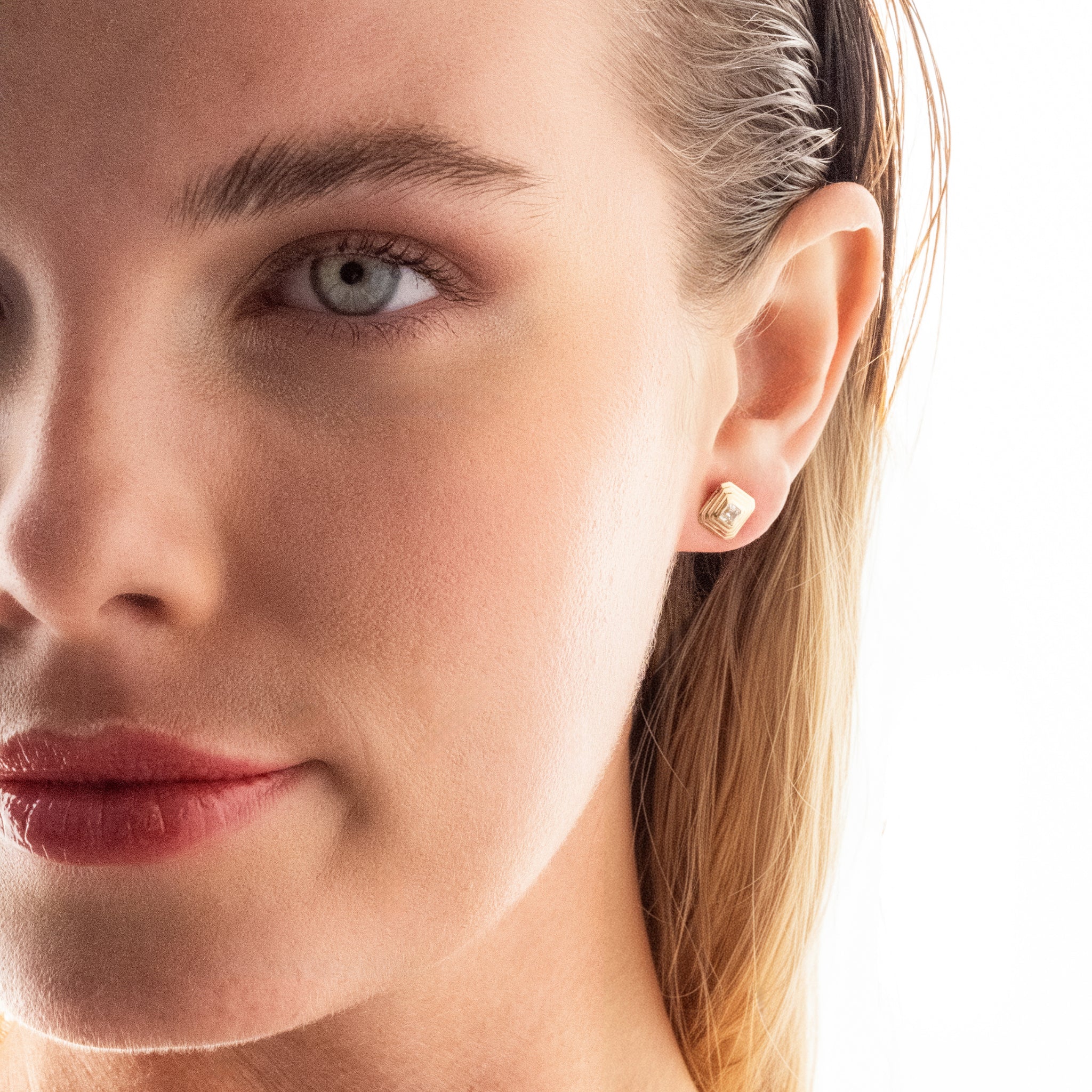 Close-up of a woman's face wearing a gold and diamond earring on a white background