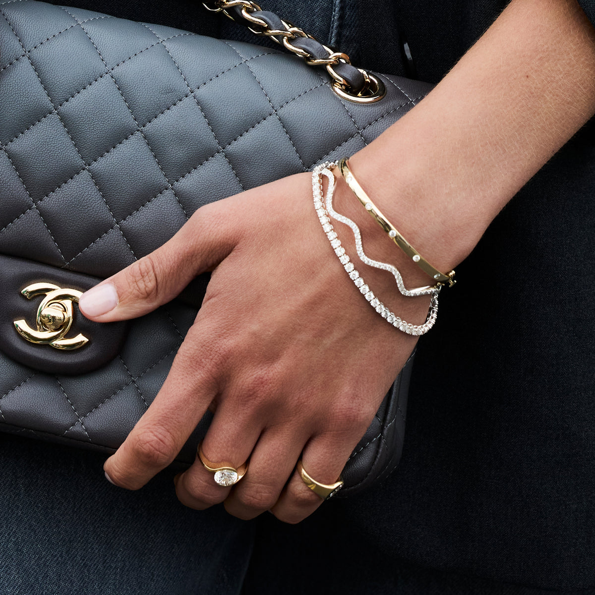 Hand wearing Diamond Wave Bangle alongside other gold bracelets, showcasing elegant style and sparkling diamonds.