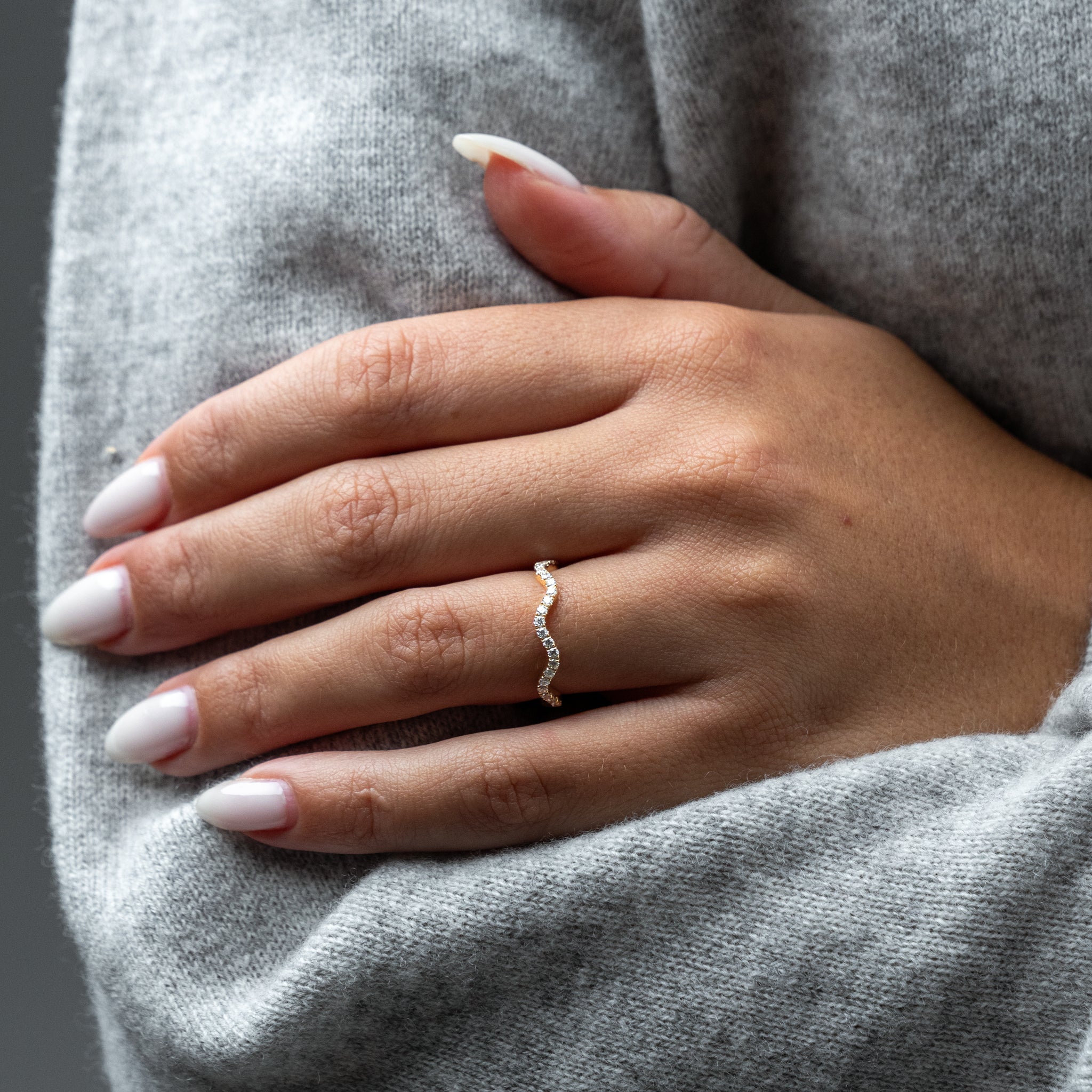 Close-up of a hand wearing a diamond ring on a gray fabric background