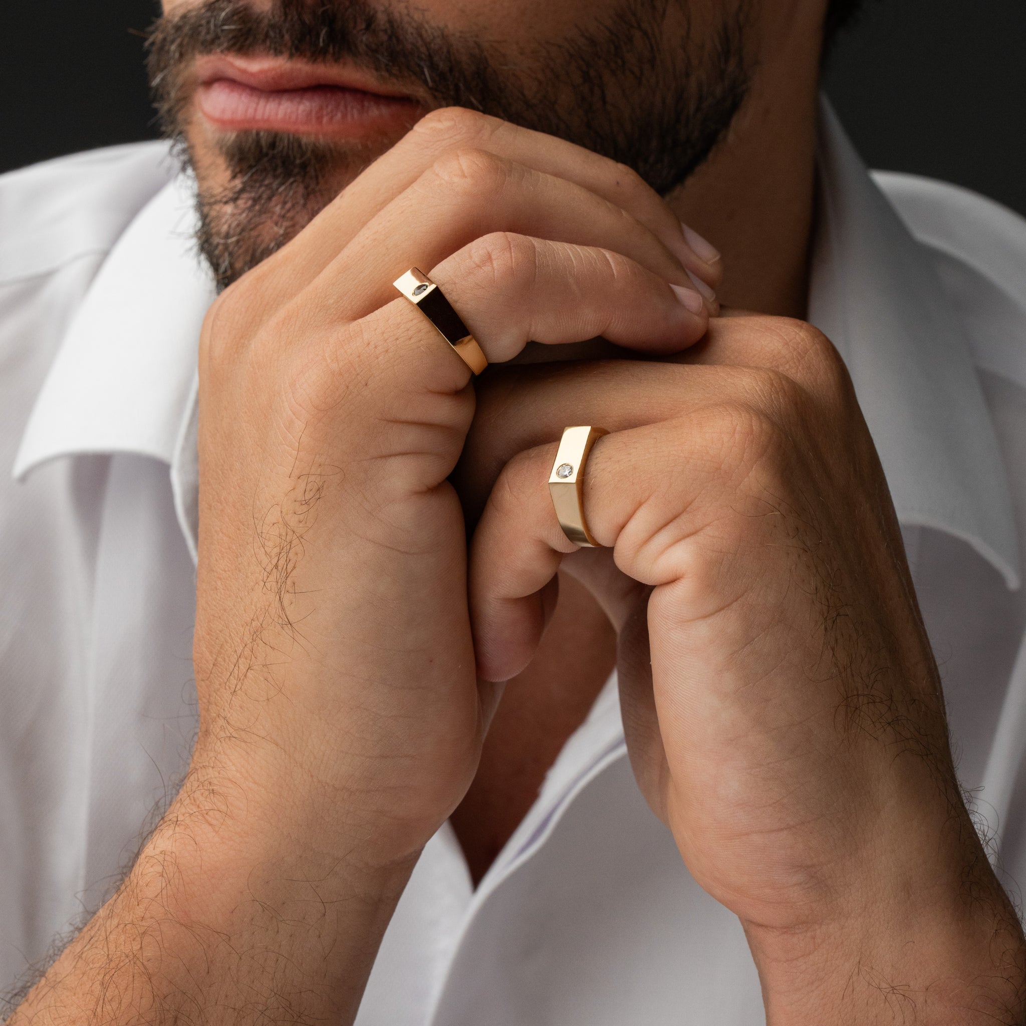 Close-up of a man's hands wearing gold rings showcasing a diamond with a dark background