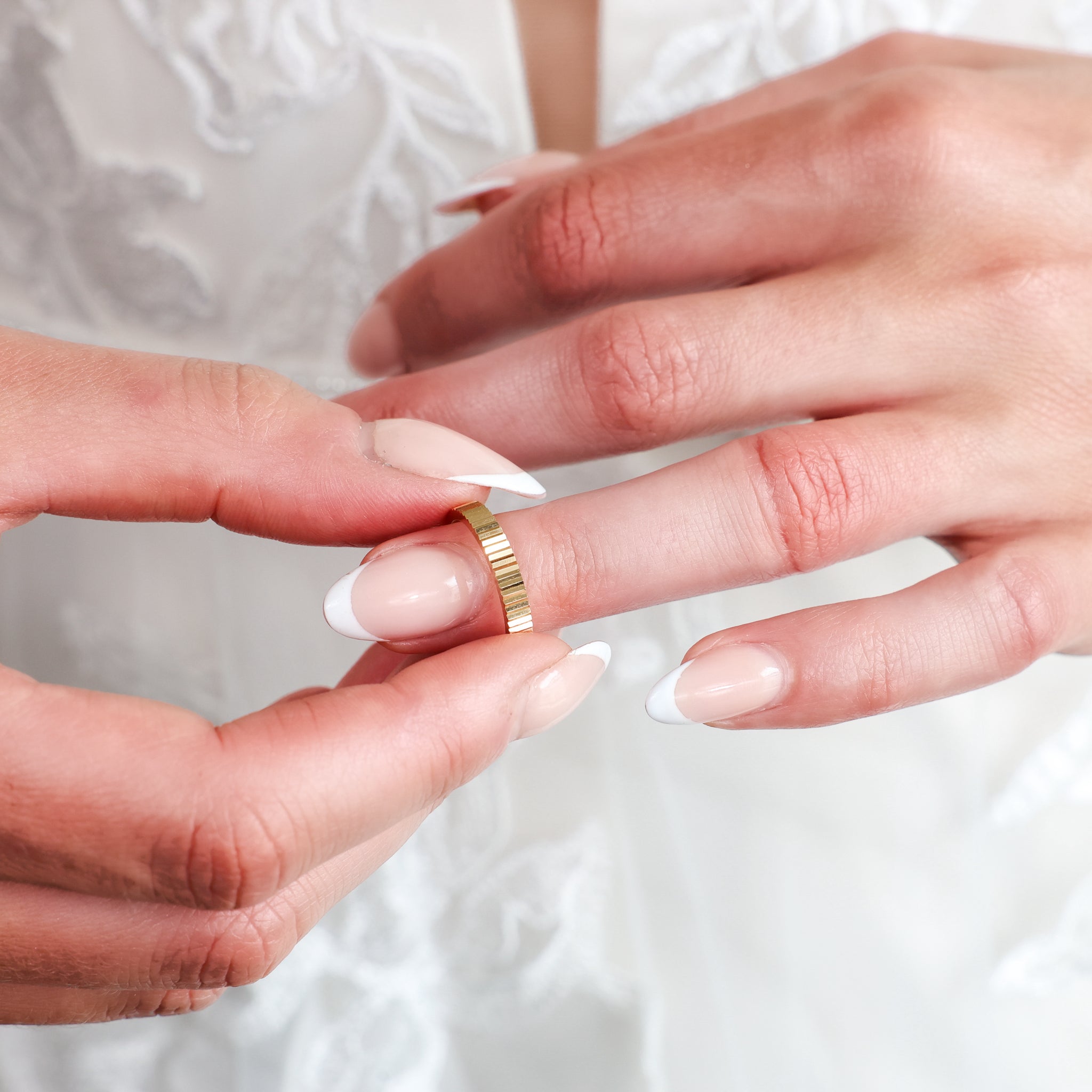 Fluted Wedding Band being placed on a finger, showcasing its clean texture and elegant design, complementing a diamond ring.
