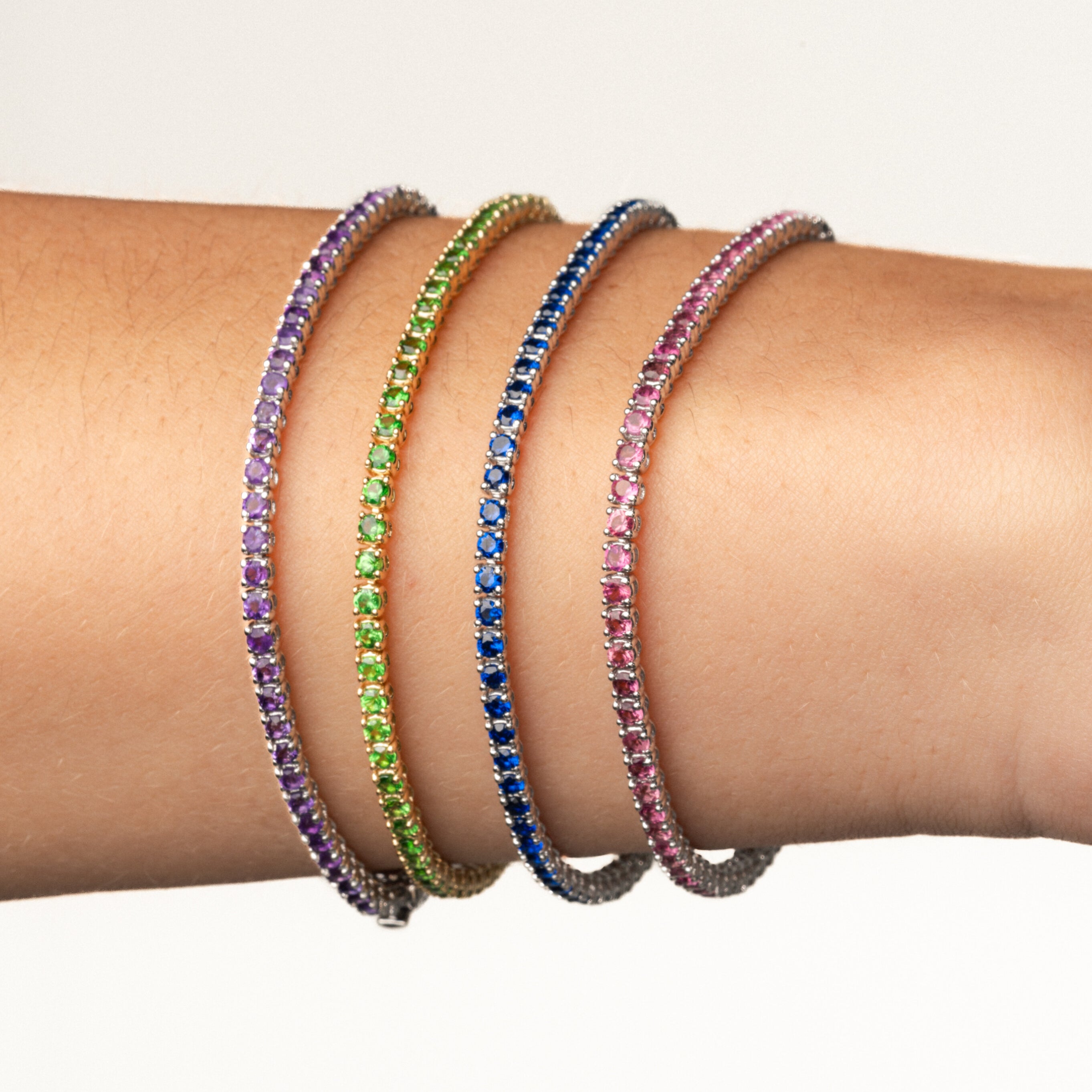 Colourful gemstone tennis bracelets displayed on a wrist showcasing elegance and luxury.
