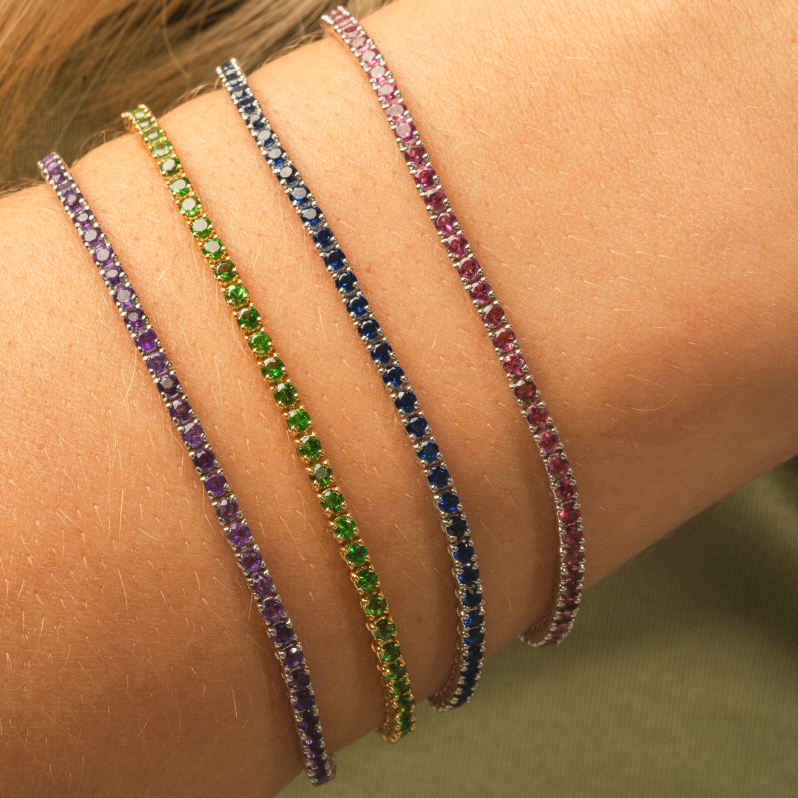 Close-up of multiple colourful gemstone tennis bracelets on a wrist showcasing vibrant hues and elegant design.