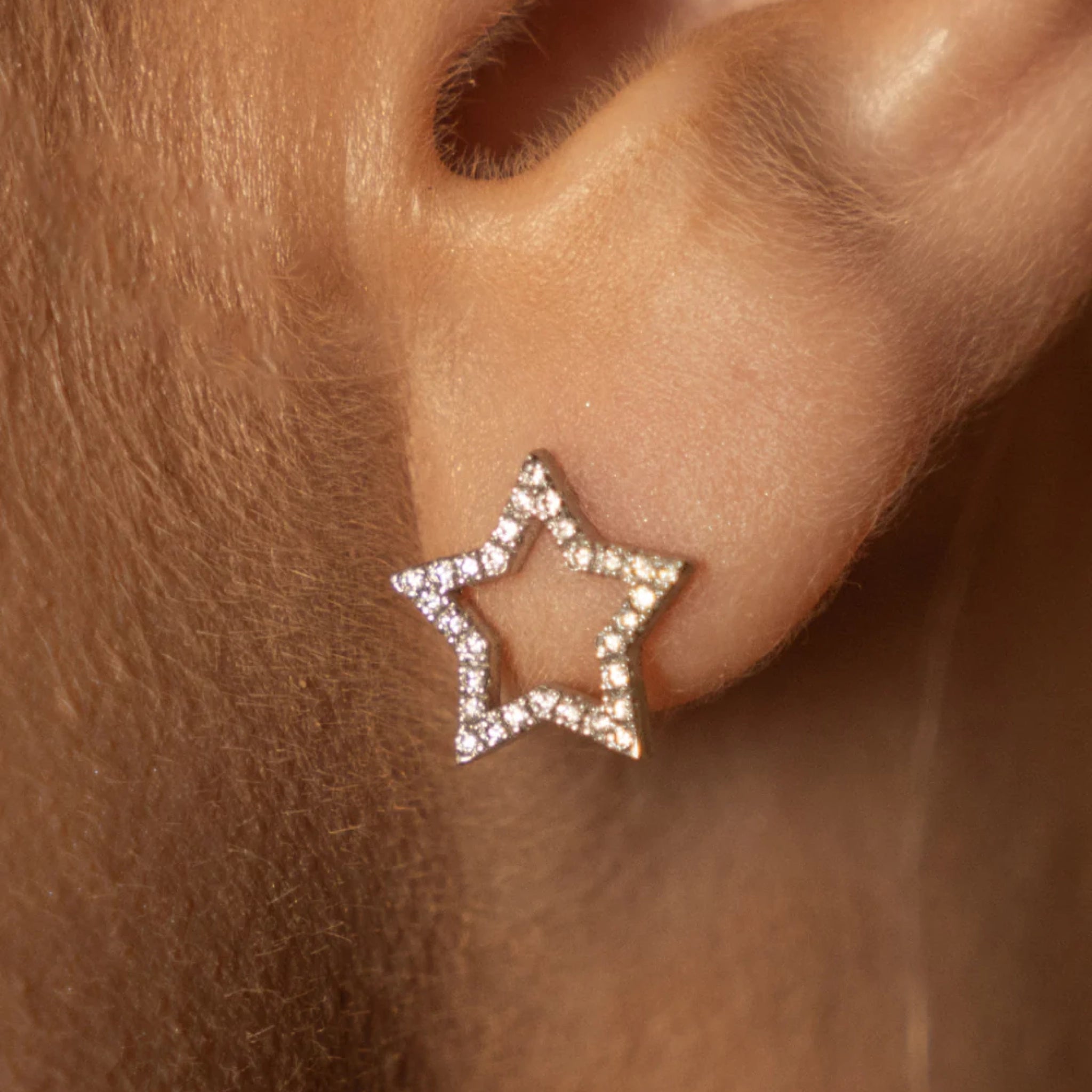 Close up of certified diamond earrings shaped like stars, set in 18ct gold, worn on earlobe.
