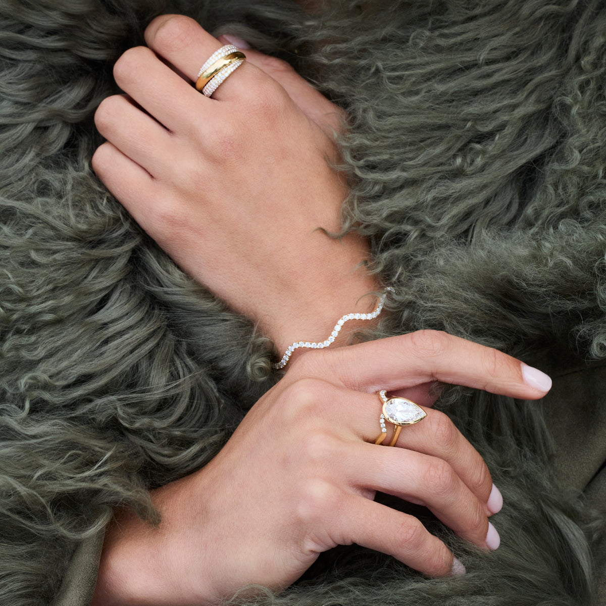 A close-up of hands featuring a 4.00ct Bezel Set Pear Shaped Ring and gold rings on a soft fur background.
