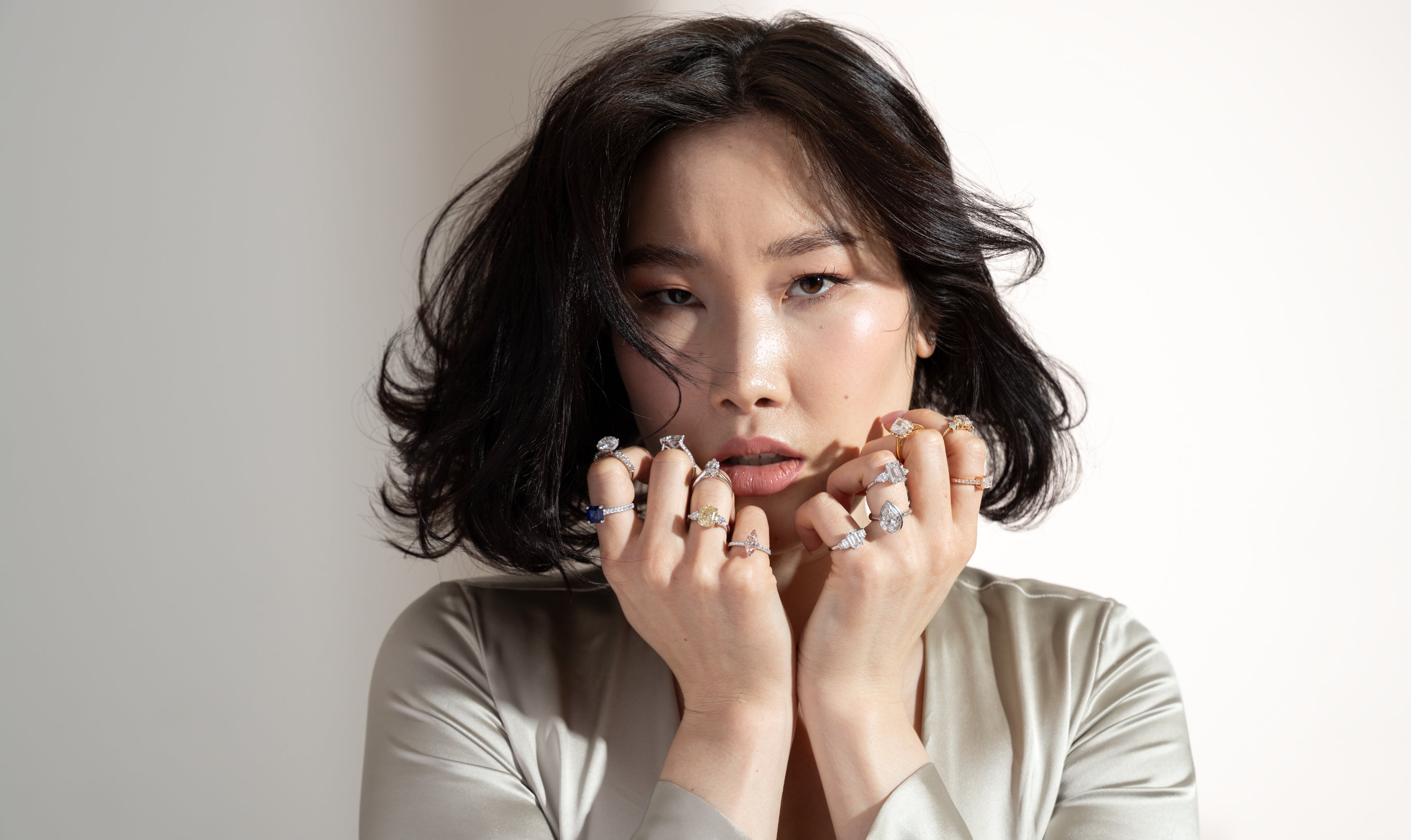 Woman wearing multiple diamond rings on a plain background