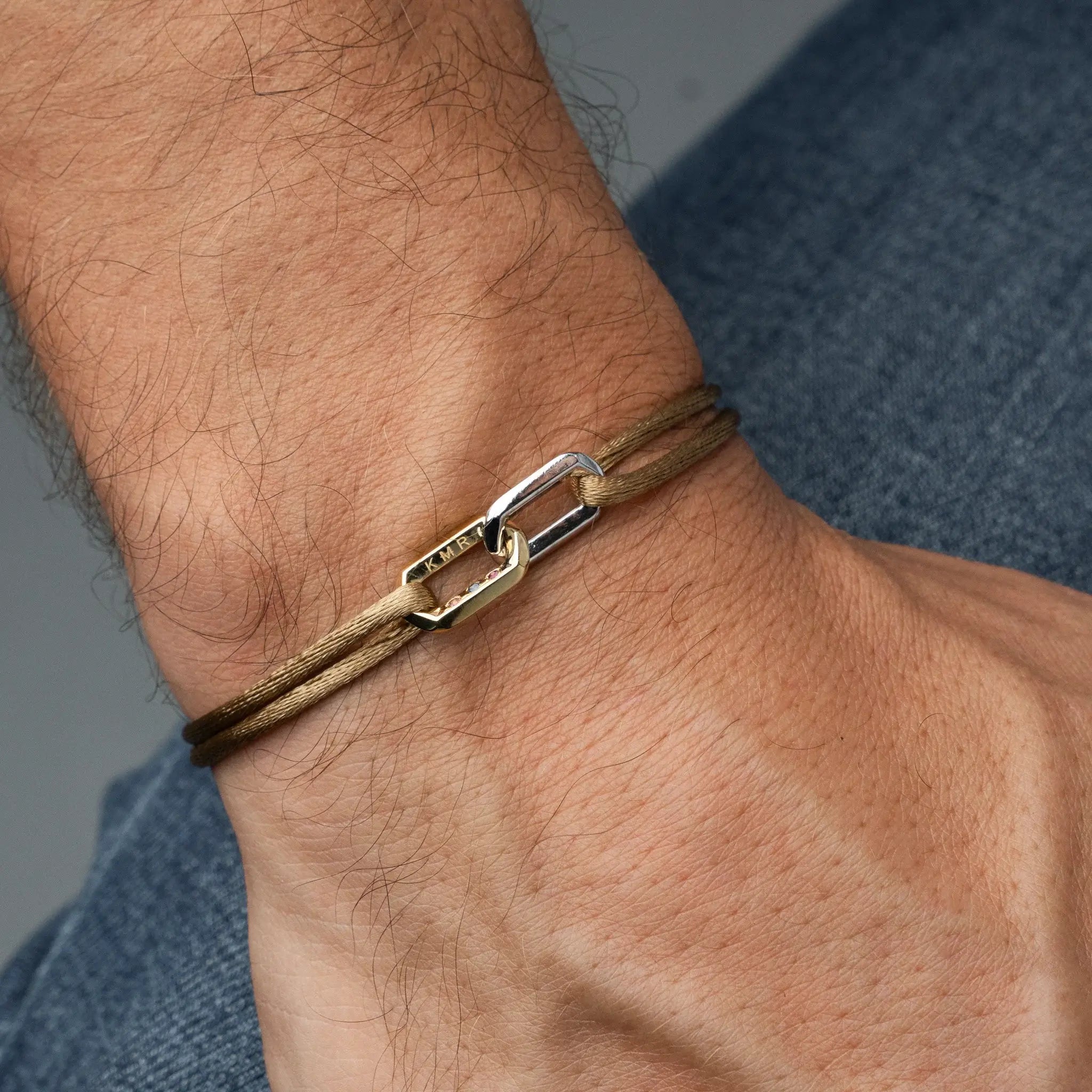 Close-up of a wrist wearing a brown leather bracelet with gold chains