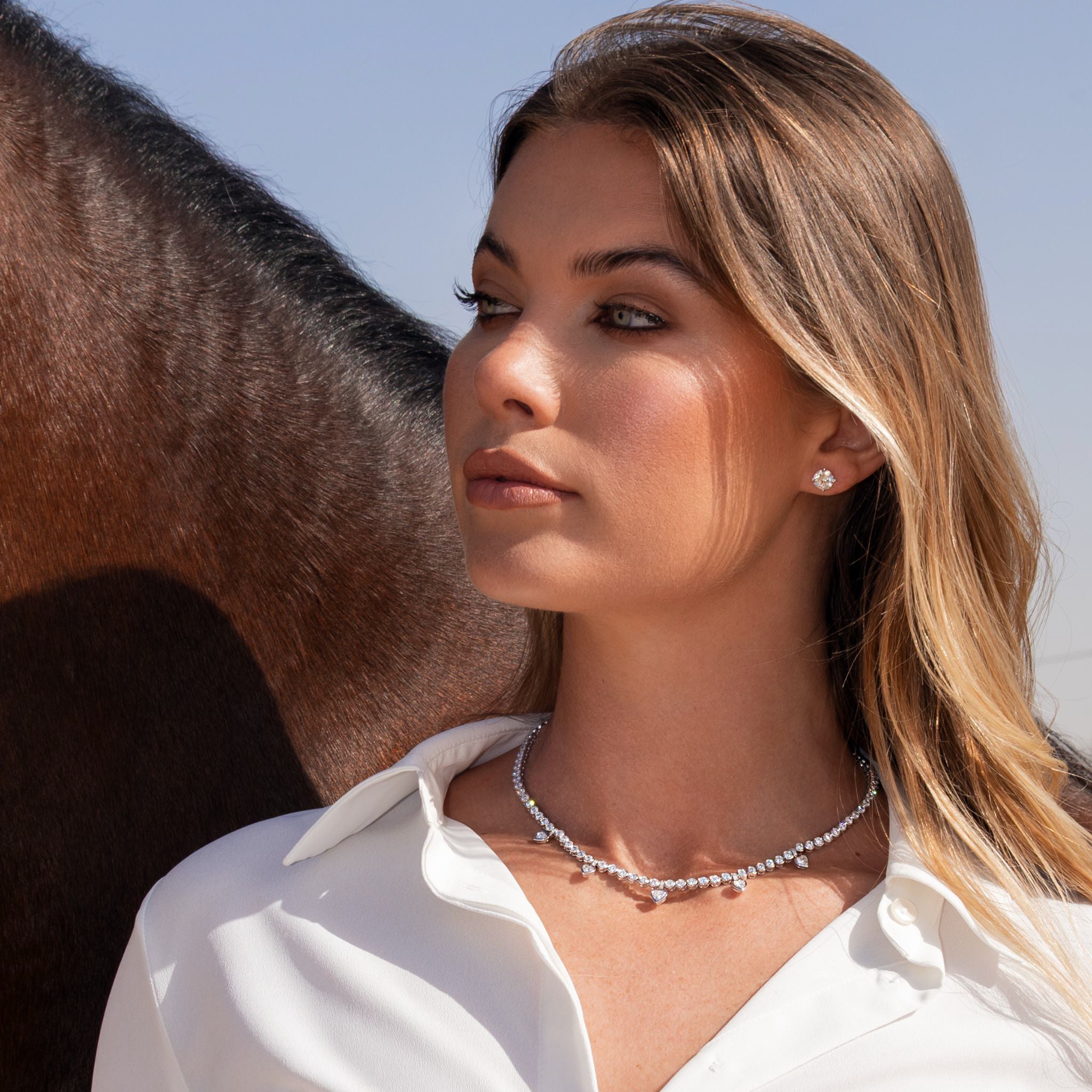 Heart Shape Diamond Tennis Necklace worn by a woman, showcasing elegant diamonds against a horse backdrop.