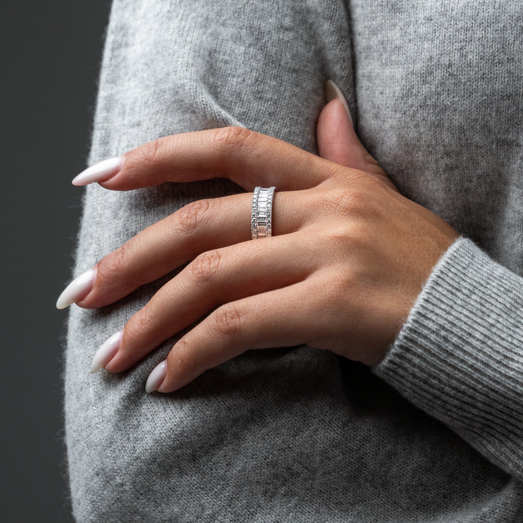 Close-up of a hand wearing a white gold ring on a gray background
