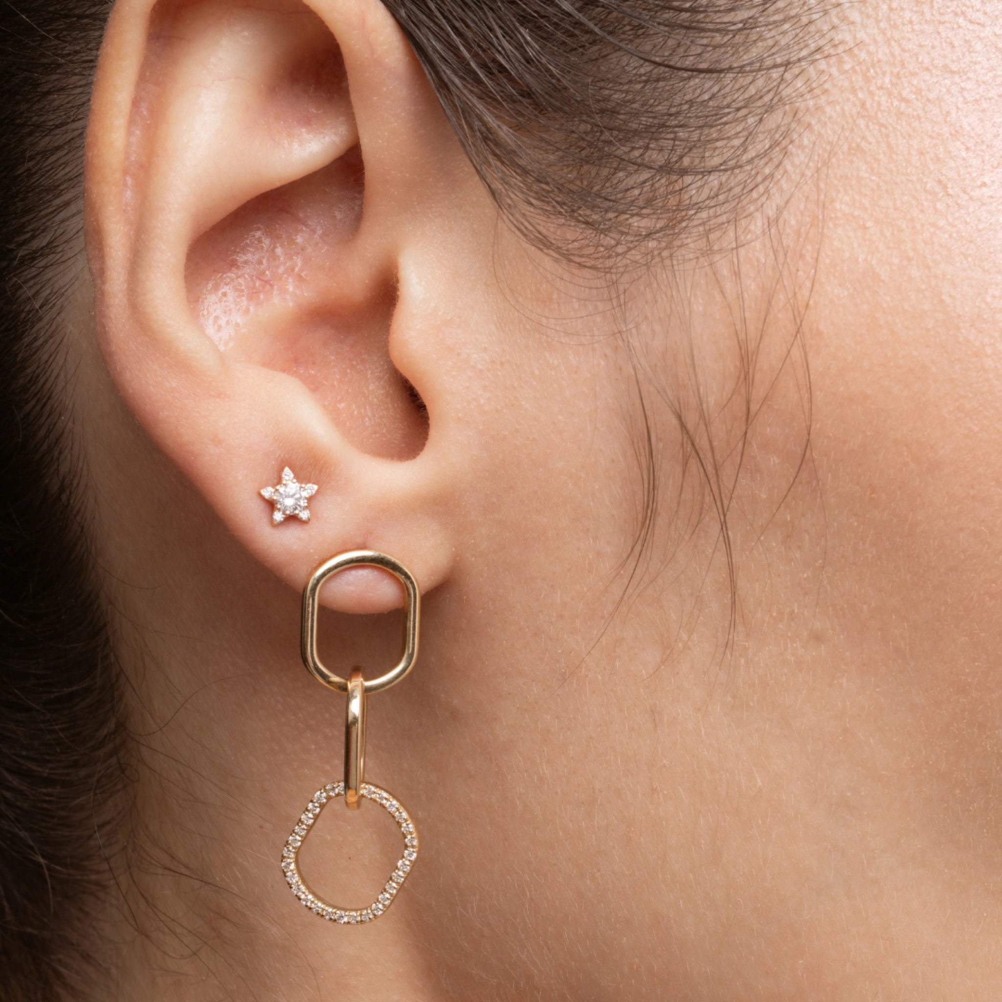 Close up of a woman's ear showcasing chain link diamond earrings and a solid gold star earring, highlighting style and elegance.
