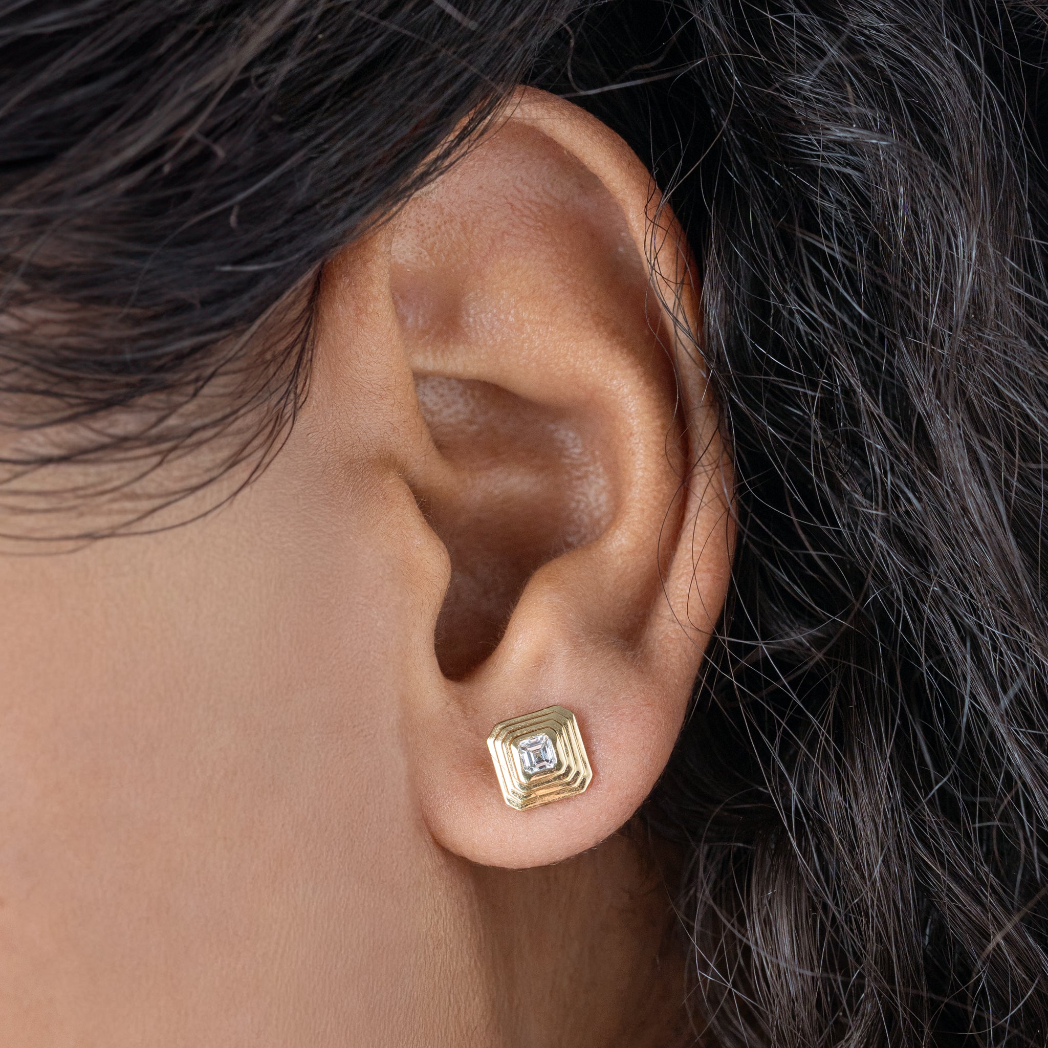 Gold earring worn on a person's ear with dark hair.